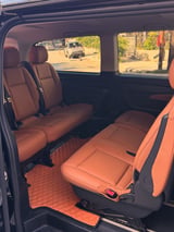Interior of a vehicle with rust-colored leather seats and orange floor mats, windows showing a street outside