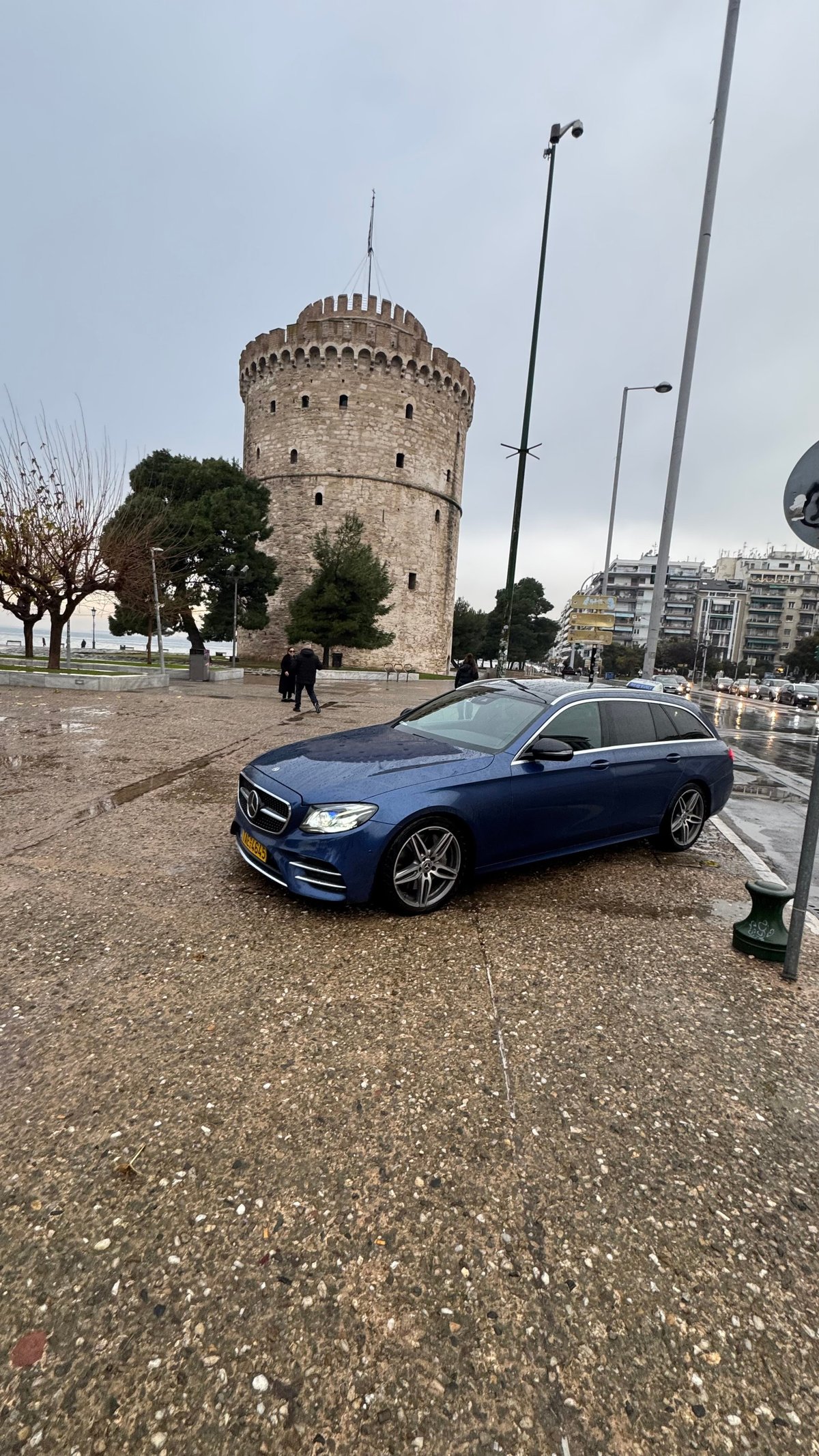 Blue Mercedes sedan parked in front of historic White Tower in Thessaloniki, Greece